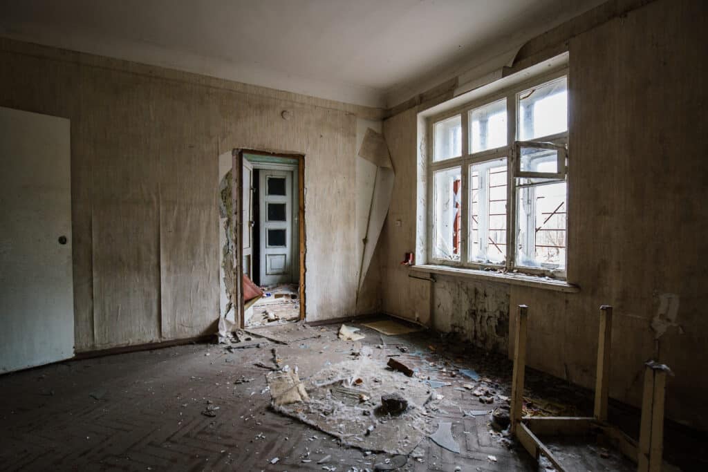 Pièce Abandonnée Sinistre : Débris, Verre Brisé Intérieur sinistre d'une pièce abandonnée, papier peint déchiré, sol jonché de débris et de morceaux de verre brisé près d'une fenêtre cassée.